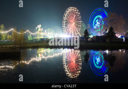 Die Lichter von zwei Riesenräder in einem Vergnügungspark spiegelt sich im Wasser eines Teiches Stockfoto