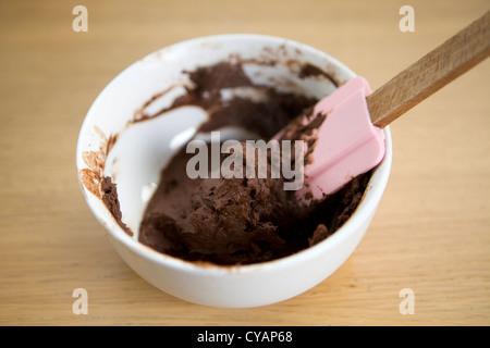 Mischen eine Paste aus Kakaopulver und Wasser in einer Schüssel mit einem Gummispachtel auf einem Holztisch. Stockfoto