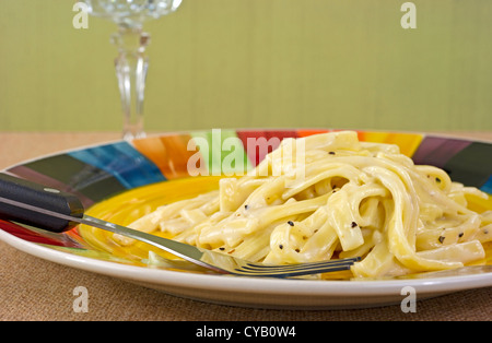 Nahaufnahme einer TV Abendessen Mahlzeit von Fettuccine Alfredo auf Teller mit Gabel mit einem Kristall-Kelch im Hintergrund. Stockfoto