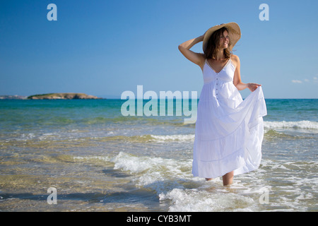 Schöne junge Frau mit einem Hut und einem weißen Kleid, spielen mit den Wellen des Meeres Stockfoto