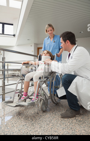 Arzt hocken neben Kind im Rollstuhl mit Krankenschwester einschieben Stockfoto