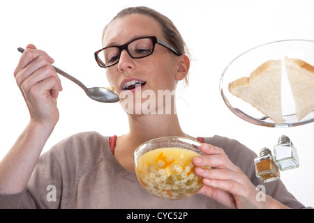 Junge Frau sitzt an einem Glastisch, Essen eine Suppe, Gemüse, Nudeln. Stockfoto