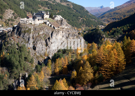 LUFTAUFNAHME. Château Queyras auf einem felsigen Sporn in einem Tal mit Lärchen und Aspen Bäumen in Herbstfarben. Château-Ville-Vieille, Hautes-Alpes, Frankreich Stockfoto