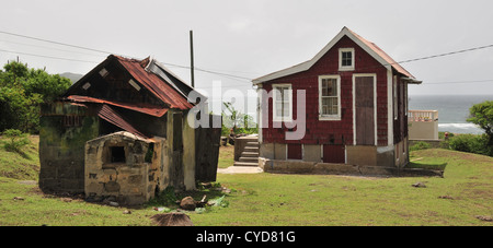 Sonnige Aussicht kleine rote Holzhaus mit Stein Nebengebäude auf dem grünen Rasen mit Blick auf Meer, Belmont, East Coast Carriacou, West Indies Stockfoto