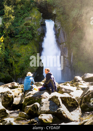 Feuerholz/Wanderer genießen Sie ein Mittagessen auf den Felsen am Riesen Tor fällt, entlang der Milford Track, Fjordland National Park, Neuseeland Stockfoto