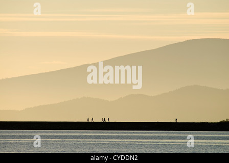 Mehrere Silhouette Menschen sind gesehen zu Fuß entlang der Iona Mole bei Sonnenuntergang in Richmond, British Columbia, Kanada. Stockfoto