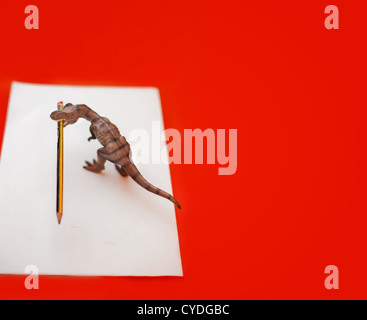 Dinosaurier Spielzeug mit einem Bleistift auf den Mund und ein weißes Blatt in einem Kinder-Schreibtisch Stockfoto