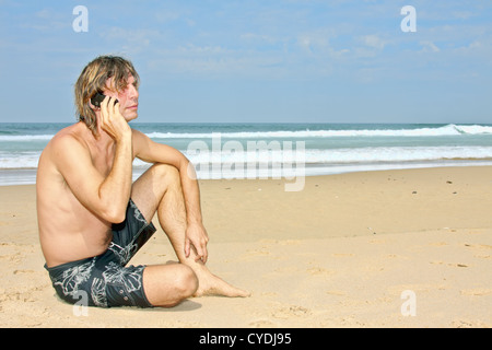 Junger Kerl sitzt am Strand telefonieren Stockfoto