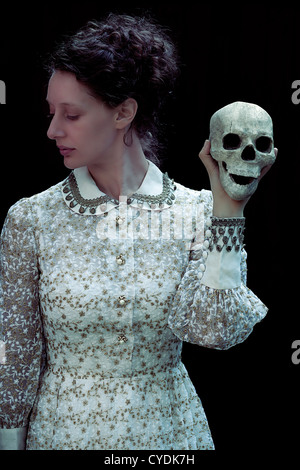 eine Frau in einem viktorianischen Kleid hält einen Schädel Stockfoto