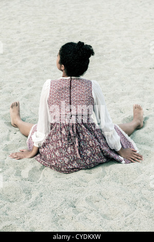 eine junge Frau in ein Vintage-Kleid am Strand sitzen
