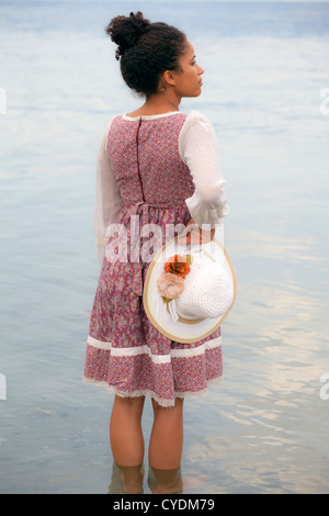eine Frau in einem geblümten Kleid hält einen Strohhut Stockfoto