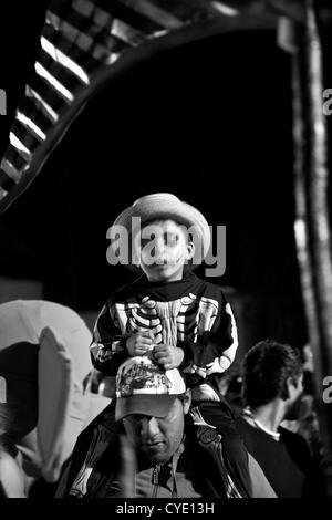 Oaxaca, Mexiko. 1. November 2012. Dia De Los Muertos feiern - Menschen im Kostüm Tanz Band in Straßen - Junge sitzt auf den Schultern der Väter Stockfoto