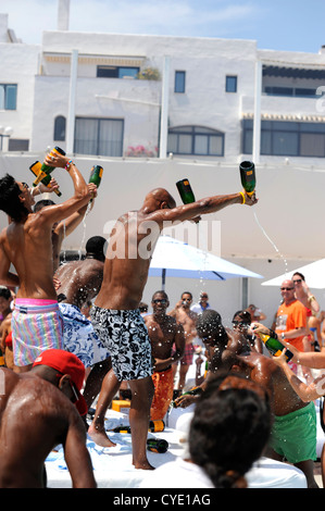 Partygänger im Beach Club Champagner Spray feiern, trinken aus Flaschen Vueve Cliquot und gießen sie über einander Stockfoto