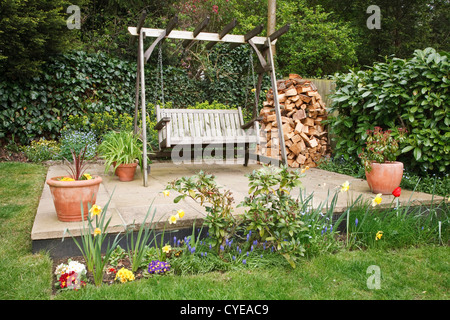 Entspannende Garten Terrasse mit Schaukel Bank, Topfpflanzen und ein Holzstapel Stockfoto