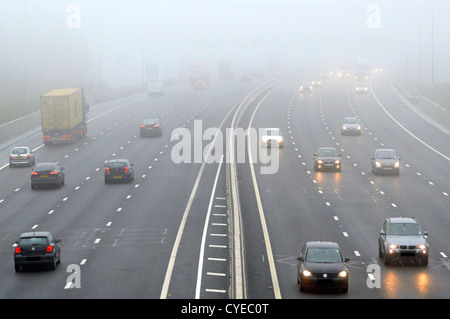 Luftverkehr mit Scheinwerfern bei dichtem Nebel auf der Autobahn M25 auf der Londoner Umlaufroute in der Nähe der Anschlussstelle 30 County of Essex England Großbritannien Stockfoto