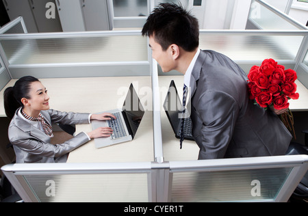 Kaufmann und Kauffrau im Büro, Mann, hält Rosen hinter Rücken Stockfoto