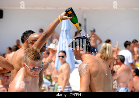 Britische Partygänger Flaschen Champagner in Strömen über einander im Beachclub Stockfoto