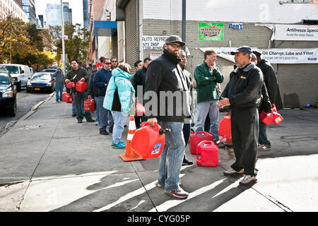 New York City, USA. 3. November 2012. Diverse gut gelaunt New Yorker tragen rote Kunststoff-Kraftstoffbehälter Line-up auf einer schönen Samstag, 3. November 2012 an einer West Side New York Mobil Station Gas für Autos & Generatoren zu kaufen Stockfoto