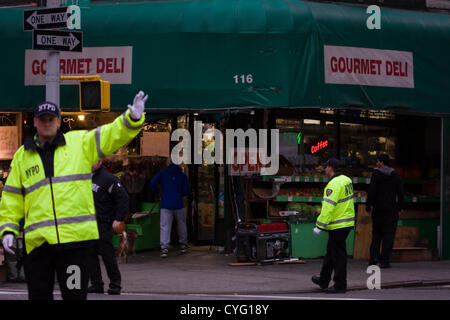 New York USA. 1. November 2012. NYPD-Polizisten tragen reflektierende Jacken direkte Zugriffe in der Abenddämmerung auf 17th Street und 7th Avenue im Stadtteil Chelsea von New York City. Ein Gourmet Deli an der Ecke ist offen für Geschäfte, nur weil es von einem roten tragbaren Generator auf dem Bürgersteig elektrischen Strom versorgt wird. Teile der Stadt bleiben dunkel wegen eines Stromausfalls in Manhattan unter 29th St vor den Auswirkungen des Hurrikans Sandy, die das Gebiet am Montag, den 29. Oktober getroffen. Stockfoto