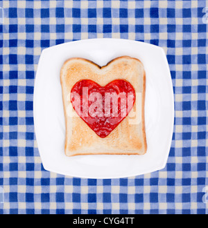 Toast mit roter Marmelade Herz auf weißen Teller dekoriert Stockfoto