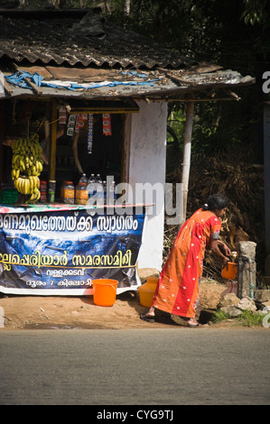 Vertikale Portrait von lokalen indischen Frau sammeln frisches Wasser aus einem Standrohr in der Mitte eine typische Straße in Munnar. Stockfoto