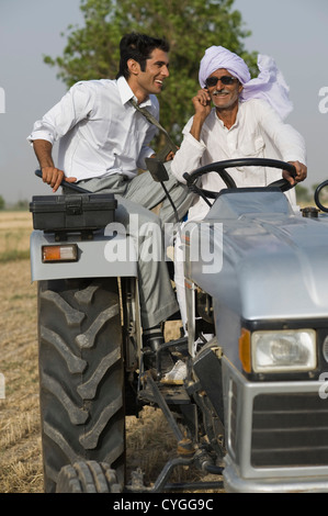 Landwirt telefonieren mit einem Handy während der Fahrt eines Traktors mit seinem Sohn Stockfoto