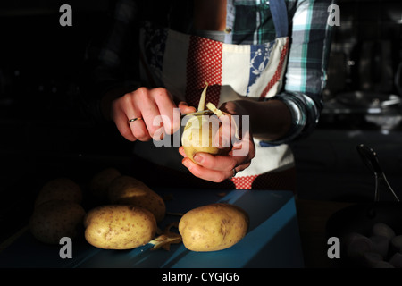 Junge Frau der 20er Jahre Altersgruppe Vorbereitung Schaben Kartoffelschälen bereit für das Kochen in der Küche Stockfoto