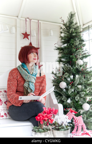 Eine junge Frau, die auf eine Weihnachtskarte zu schreiben, während der Blick aus dem Fenster Stockfoto