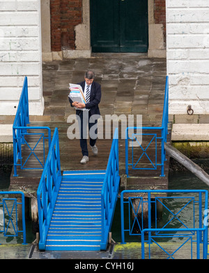 Ein Herr in einem Business-Anzug tragen ein Bündel Papiere zu Fuß entlang einer Anlegestelle um ein Boot in Venedig Stockfoto