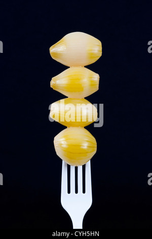 4 eingelegte Zwiebeln auf weißem Kunststoff Gabel, schwarzer Hintergrund Stockfoto