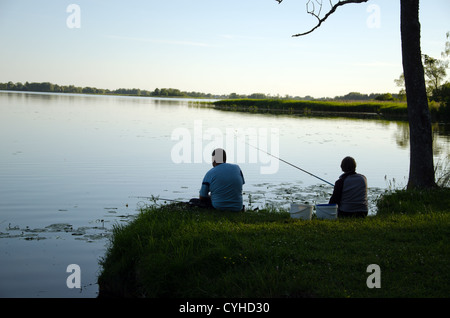 Romantische Paar sitzen am Ufer des Sees mit Ruten Angeln Angeln im schönen Abend. Stockfoto