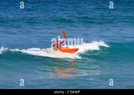 Mann in einem Wildwasser Einerkajak eine trockene Ober- und Helm tragen, wie er die Welle reitet Stockfoto