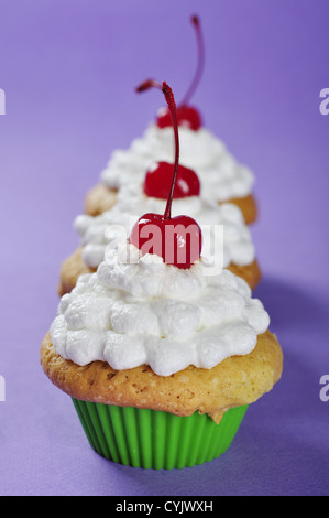 Muffins mit Sahne und Kirsche in Reihe auf violettem Hintergrund Stockfoto