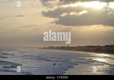 Zwei entfernte Surfer in einem silbernen Meer bei Sonnenuntergang bei Folly Beach, SC als Hurrikan Sandy beginnt Affest der Brandung Stockfoto