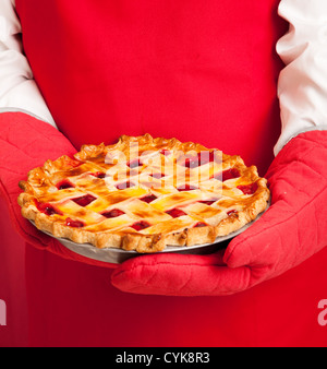 Nahaufnahme eines Bäckers in Topflappen, Hände halten einen frischen Kirschkuchen. Stockfoto