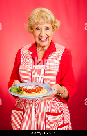 Süße Retro-Großmutter hält einen Teller mit frischen, heißen italienische Spaghetti marinara Sauce. Roten Hintergrund. Stockfoto