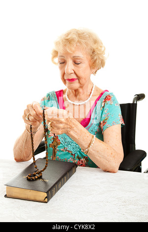 Ältere katholische Großmutter im Rollstuhl mit Rosenkranz zu beten. Weißen Hintergrund. Stockfoto