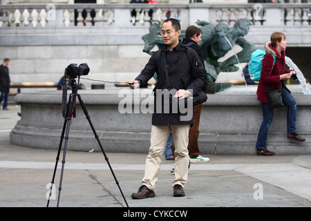 Ein Mann mit einem Stativ und Kabel lösen, nehmen Sie ein Foto von sich selbst auf dem Trafalgar Square, London Stockfoto