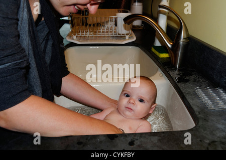 Ein sechs Monate altes Baby Boy wird gebadet in der Küchenspüle Stockfoto