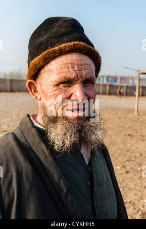 Alten Uiguren Mann Porträt mit Pelzmütze und Bart auf Mal Basar Vieh Wochenmarkt. Kashgar, Xinjiang, China Stockfoto