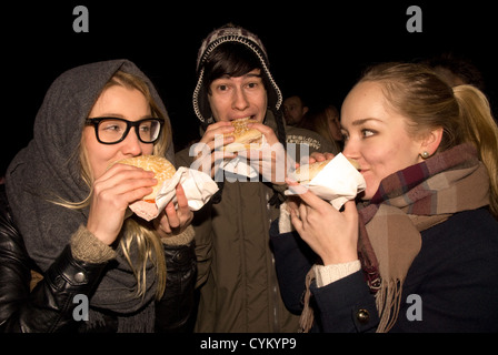 Drei junge Menschen essen hog Roast an einem Lagerfeuer Nacht Anzeige, chiddingfold, Surrey, UK. November 2012. Stockfoto