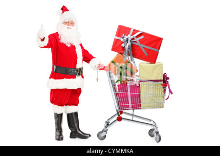 Santa Claus isoliert halten einen Einkaufswagen voller Geschenke und einen Daumen aufgeben auf weißem Hintergrund Stockfoto