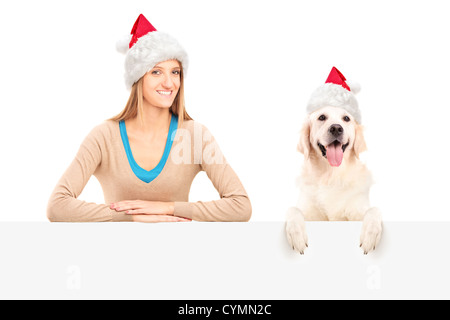 Lächelnde Frau und Hund Santa Claus Hüte tragen und posiert hinter eine Blindplatte Stockfoto