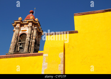 Mexiko, Bajio, San Miguel de Allende, Teil Blick auf helle gelbe Außenwand und Kirchenglocke Turm mit blauem Himmel. Stockfoto