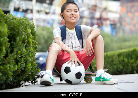 Schüler sitzen auf Skateboard mit dem Fußball in der hand Stockfoto