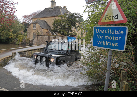 Ein Land Rover Defender beenden einen überfluteten Ford auf dem River Windrush, Bourton auf dem Wasser, Gloucestershire, UK. Stockfoto