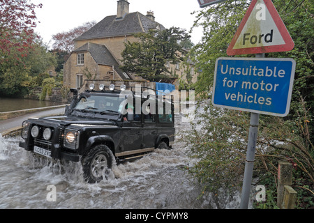 Ein Land Rover Defender beenden einen überfluteten Ford auf dem River Windrush, Bourton auf dem Wasser, Gloucestershire, UK. Stockfoto