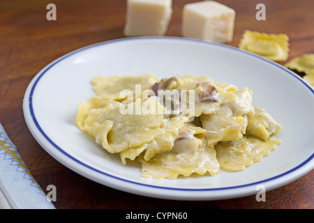 Teller mit Ravioli mit Pilzen und Käse umgeben von Rohstoffen Stockfoto