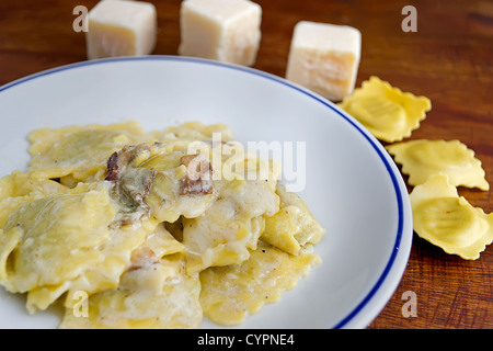 Teller mit Ravioli mit Pilzen und Käse umgeben von Rohstoffen Stockfoto