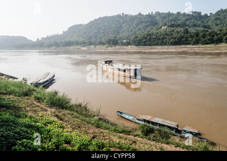 Hua Hang Thom überdachtes Holzboot Mekong Fluss Luang Prabang Laos / LUANG PRABANG, Laos — Ein überdachtes hua Hang thom, oder großes Langboot, navigiert den Mekong Fluss nahe Luang Prabang. Diese Holzschiffe dienen als wichtige regionale Fähren, die entlegene Gemeinden entlang der Wasserstraße verbinden. Die verlängerte Dachkonstruktion bietet notwendige Unterschlupf für den Fernverkehr und bietet Platz für Passagiere und Vorräte auf Reisen wie der mehrtägigen Route zwischen Luang Prabang und Huay XAI nahe der thailändischen Grenze. Stockfoto